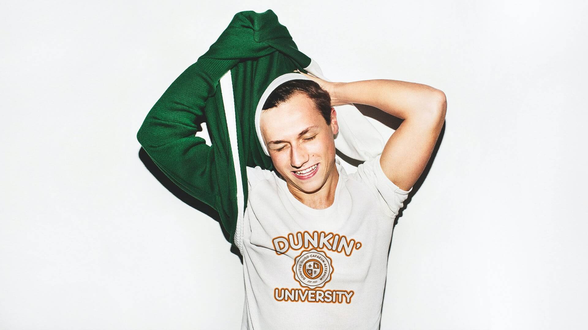 A person in a white Dunkin' Donuts tshirt who is taking off a green sweatshirt