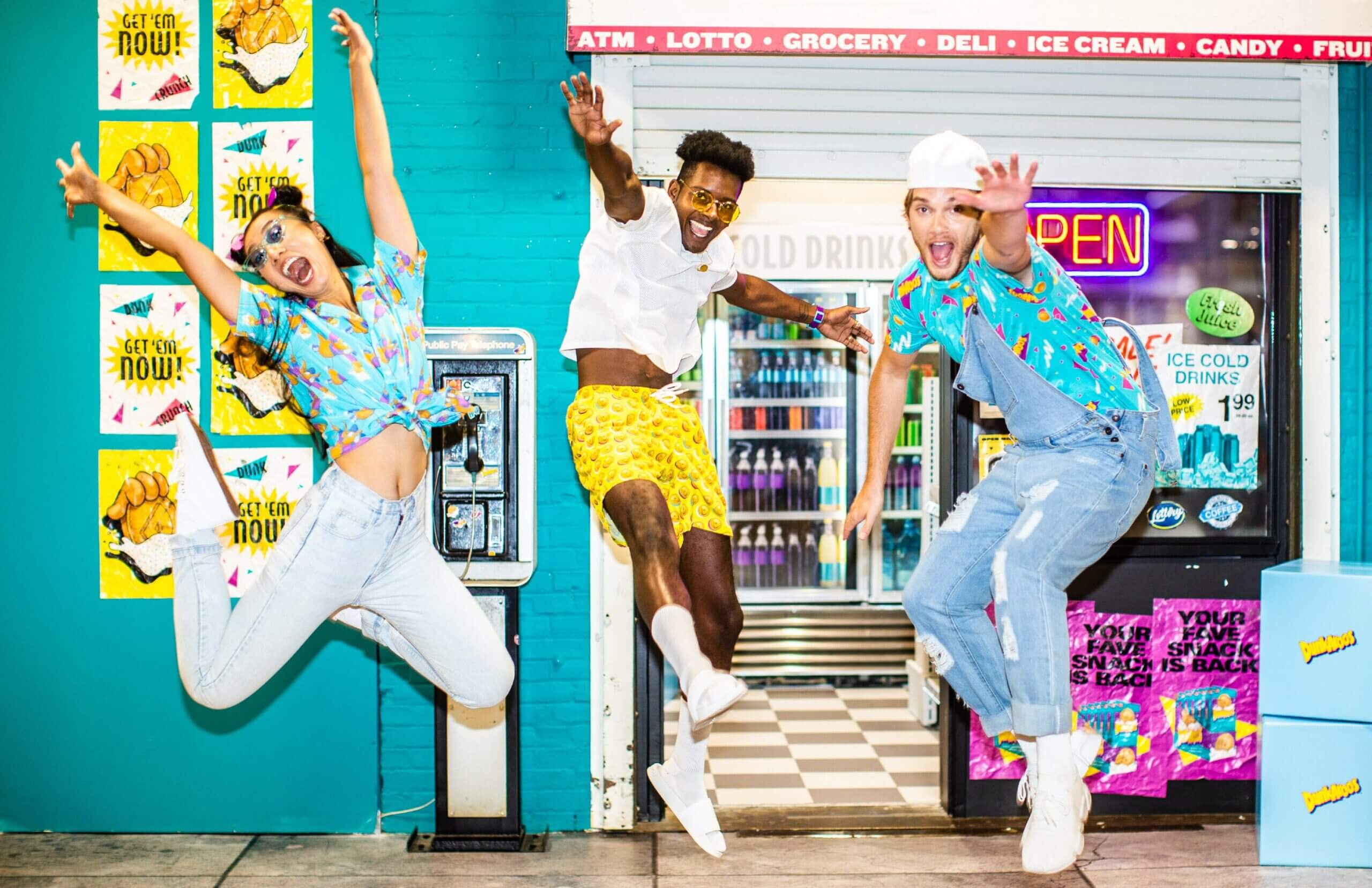 Three people in DunkAroos branded apparel jumping for joy in front of an arcade