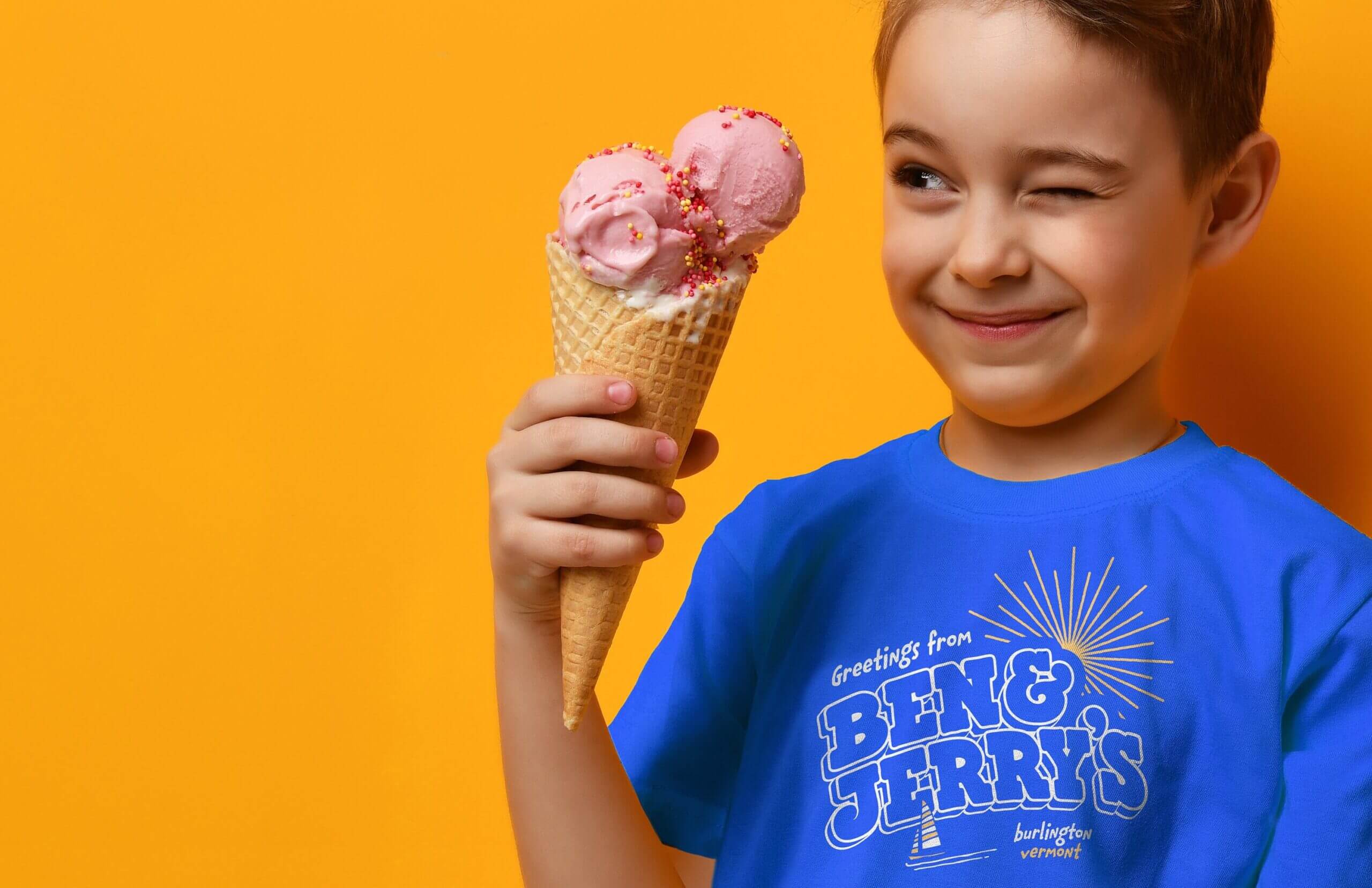 Child holding a waffle ice cream cone and staring at it with one eye open